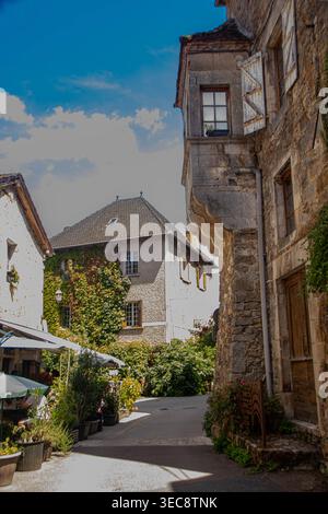 Malerische mittelalterliche Gasse in Martel, Frankreich, mit einem Steinturm, Cafétischen im Freien und üppigem Efeu auf alten Gebäuden Stockfoto