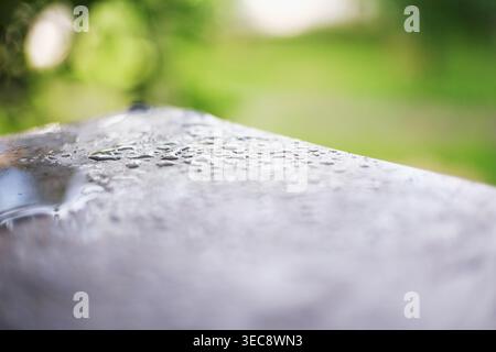 Wassertropfen auf glatter Oberfläche mit grünem Bokeh-Hintergrund, Makrodetails Stockfoto