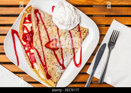 Süße Crepes gefüllt mit Erdbeeren und garniert mit Beerensauce und Schlagsahne. Stockfoto