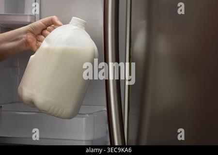 Horizontale Nahaufnahme der Hand, die zu Hause Milchkännchen aus dem Kühlschrank nimmt Stockfoto