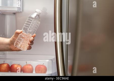 Horizontale Nahaufnahme der Hand, die zu Hause eine Flasche Wasser aus dem Kühlschrank nimmt Stockfoto
