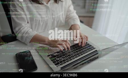 Ein fokussierter, individueller Typ auf einem schlanken Laptop, umgeben von einem modernen Arbeitsbereich. Die Überlagerung von Codierungssymbolen repräsentiert die Welt der Softwareentwicklung Stockfoto
