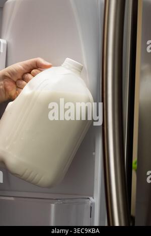Vertikale Nahaufnahme der Hand, die Milchkännchen von der Kühlschranktür zu Hause nimmt Stockfoto