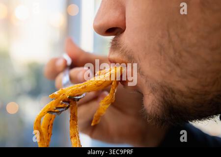 Der Mann isst fette Pasta, saugt sie mit dem Mund. Konzept von Übergewicht, Diabetes, Völlerei, Diabetes, Überernährung, Nahaufnahme seines Kaumundes Stockfoto