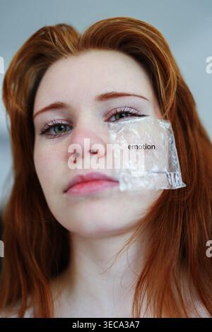 Nahaufnahme Porträt der rothaarigen Frau mit transparentem Patch auf Gesicht beschriftet Emotion, konzeptionelle psychische Gesundheit und Identitätsthema. Stockfoto