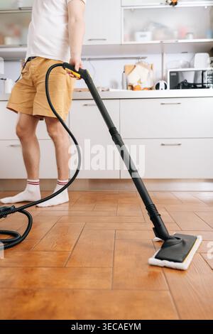 Vertikaler zugeschnittener Schuss von nicht erkennbarem Mann, der Dampfreiniger verwendet, um Küchenboden zu desinfizieren und zu reinigen, Hausarbeit für Stockfoto