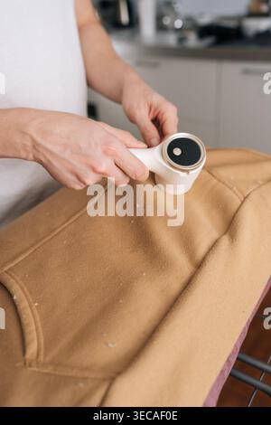 Vertikale Nahaufnahme einer Person mit elektrischem Stoffrasierer, um Fussel und Fuzz von braunem Sweatshirt zu entfernen, um eine glatte Textur wiederherzustellen und erfrischt zu werden Stockfoto