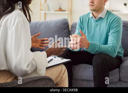 Psychologin berät jungen Mannpatienten, der während der Therapiesitzung in der Praxis auf dem Sofa sitzt. Stockfoto