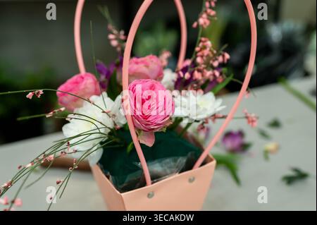 Nahaufnahme eines wunderschönen Blumenstraußes mit rosa Ranunkeln und weißen Chrysanthemen in einer pinkfarbenen Papiertüte mit Griffen an einem Arbeitsplatz in einer Blume Stockfoto