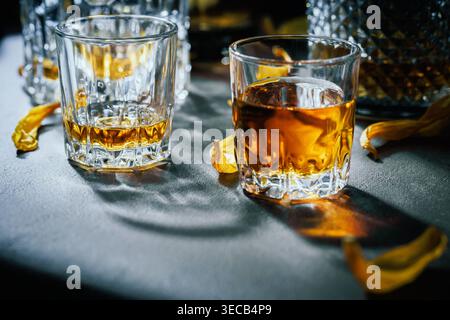 Zwei Whiskey-Gläser mit Bernsteingetränk und gelben Blütenblättern auf dramatischer Tischplatte Stockfoto