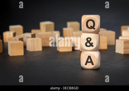 Gestapelte Holzblöcke mit den Buchstaben Q und A zwischen verstreuten leeren Würfeln auf dunklem Hintergrund. Konzept für Fragen, Antworten und FAQ. Stockfoto
