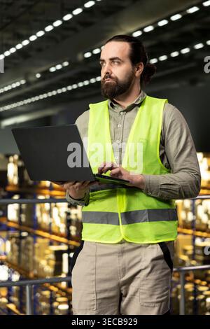 Logistikmitarbeiter, die im Lager mit Laptop für die Verteilung und den Versand arbeiten und die Paketkontrolle im Lagerraum unterstützen. Lieferkettenprozess in großen Geschäftsstandorten. Stockfoto