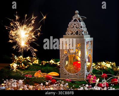 Weihnachtsdekoration mit leuchtendem Glitzer, Kerzen, einer Laterne, Tannenzweigen, Kegeln und getrockneten Orangenscheiben, Komposition Stockfoto