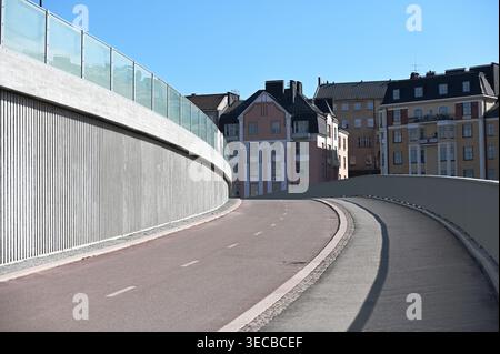 Gekrümmte Straße und Fußgängerweg auf einer modernen Brücke in Helsinki, Finnland, führt zu farbenfrohen Wohnhäusern unter einem klaren blauen Himmel, hoch Stockfoto