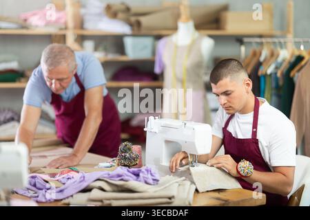 Der junge Mann näht sich maschinell männliche Assistenten-Zeichenmuster an Stockfoto