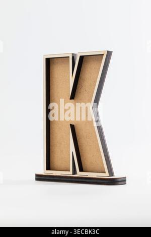 Der minimalistische Holzbuchstabe „K“ steht aufrecht. Hellbraune Körnung steht im Kontrast zu dunklen Kanten. Sauberer weißer Hintergrund verbessert die moderne Ästhetik. Perfekt für Stockfoto