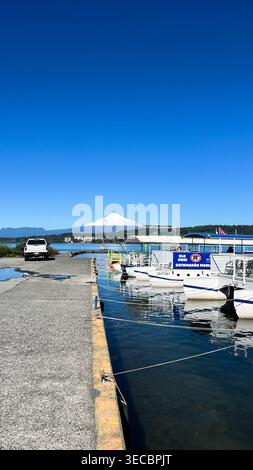 Der Hafen am Villarric-See mit Touristenbooten, die friedlich entlang des Hafens und dem majestätischen, schneebedeckten Vulkan Villarrica anlegen. Stockfoto