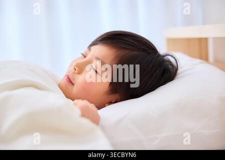 Friedlicher japanischer Junge, der ruhig auf einem Bett mit natürlichem Licht schläft Stockfoto