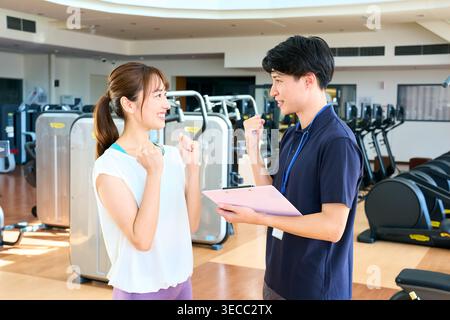 Japanischer junger männlicher Personal Trainer und weibliche Kundin, die in einem Fitnessstudio Eingeweide posiert und lächelt Stockfoto