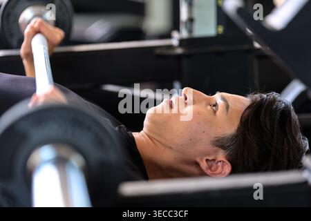Zielgerichteter junger japanischer Mann, der in einem Fitnessstudio eine Tischpresse durchführt Stockfoto