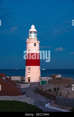 Ein markanter Leuchtturm mit einem rot-weißen Bänderturm steht am Europa Point in Gibraltar, der während der Dämmerung beleuchtet wird. Die Szene fängt das Licht ein Stockfoto