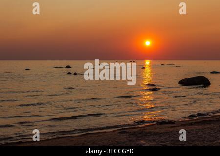Roter Sonnenuntergang über der Ostsee mit strahlender Sonnenspiegelung, ruhigen Wellen und felsiger Küste, friedlicher abendlicher Meereslandschaft Stockfoto