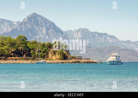 Yachten in der Nähe der kleinen Halbinsel in Kemer, Antalya, Türkei, türkisfarbenes Meer mit Bergen im Hintergrund, sommerliche Küstenlandschaft Stockfoto