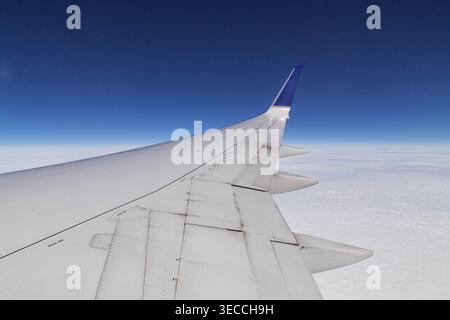 Blick von einem Flugzeugfenster aus auf einen Boeing 737 Flügel und Winglet, der über einer dicken Schicht weißer Wolken unter einem klaren blauen Himmel fliegt Stockfoto