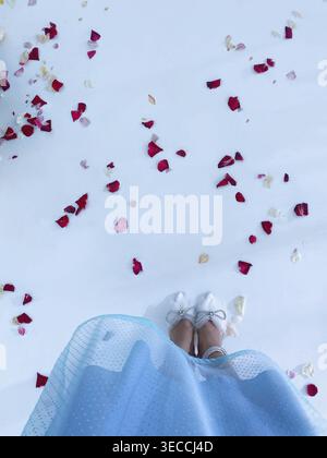 Frau im Kleid, die auf weißem Boden steht, mit Blütenblättern, sanftem Licht, romantischer Ästhetik Stockfoto