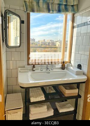 Modernes Badezimmer mit Waschbecken unter dem Fenster, Tageslicht und Stadtblick, minimalistisches Design in neutralen Farben Stockfoto