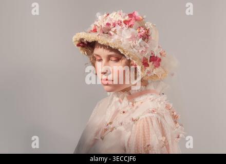 Die Models junger Frauen haben einen raffinierten Blumenhut und ein transparentes, im Vintage-Stil inspiriertes Oberteil in einem hellen Studio Stockfoto