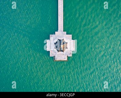 Von oben nach unten auf den einzigartigen sechseckigen Pavillon am Ende eines langen weißen Piers, der sich in lebendiges grünes Wasser erstreckt Stockfoto