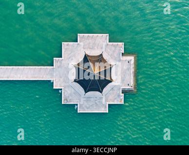 Von oben nach unten auf den einzigartigen sechseckigen Pavillon am Ende eines langen weißen Piers, der sich in lebendiges grünes Wasser erstreckt Stockfoto