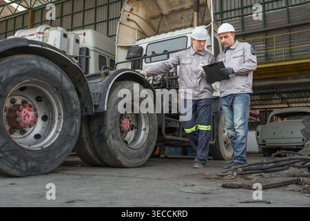 Kaukasische und mittelgroße männliche Techniker aus dem Nahen Osten gehen durch einen asiatischen Containerhof, während sie ein Klemmbrett halten, das für Routineinspektionen steht Stockfoto