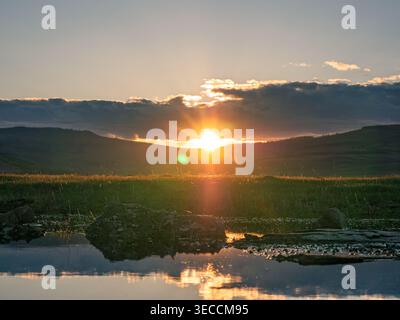 Sonnenaufgang über Hügeln und Reflexion im Wasser während der frühen Morgenstunden in einer natürlichen Umgebung Stockfoto