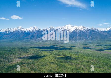 Panoramablick auf majestätische, schneebedeckte Berge ragen an einem sonnigen Tag über einer weiten grünen Ebene Stockfoto