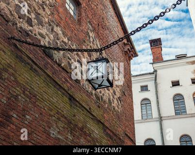 Eine Vintage-Laterne aus Metall hängt an einer schweren Kette an einer verwitterten Mauerwand aus Ziegeln und Stein und zeigt europäische Architektur Stockfoto