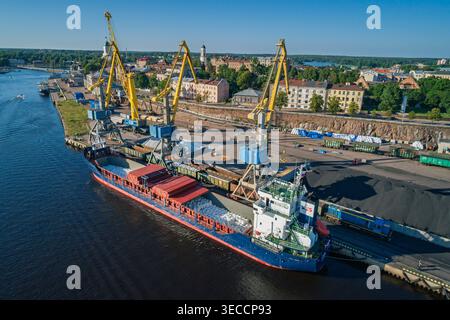 Massengutschiffen an einem Industriehafen angedockt, große gelbe Kräne und Zugwagen transportieren die Fracht bei Tageslicht Stockfoto