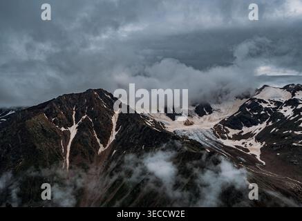 Bergkette, teilweise bedeckt von Wolken und Schnee in der Nähe eines Gletschers an einem bewölkten Tag im Kaukasus Stockfoto