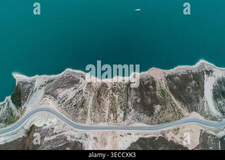 Aus der Vogelperspektive fängt die gewundene Straße ein, die die zerklüftete Küste des Kazenoy Sees mit blauem Wasser durchzieht Stockfoto