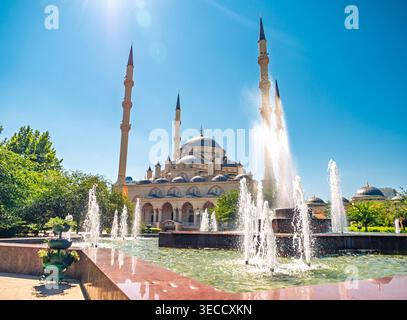 Grosny, Russland - 30. Juli 2021: Akhmad-Kadyrow-Moschee mit großen Minaretten und zentraler Kuppel, die sich in einem hellen Brunnen unter klarem Himmel spiegelt Stockfoto