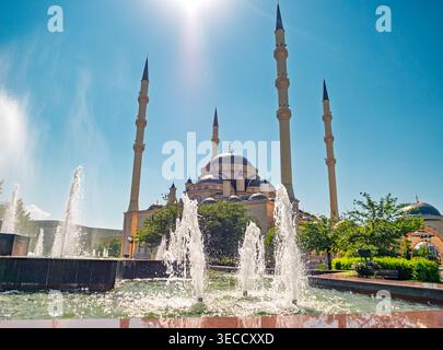 Grosny, Russland - 30. Juli 2021: Akhmad-Kadyrow-Moschee mit großen Minaretten und zentraler Kuppel, die sich in einem hellen Brunnen unter klarem Himmel spiegelt Stockfoto
