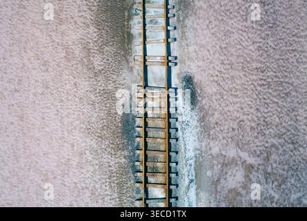 Alte Bahnschwellen und Schienen überqueren eine riesige rosa Salzebene und zeigen Strukturen und Muster aus der Vogelperspektive Stockfoto