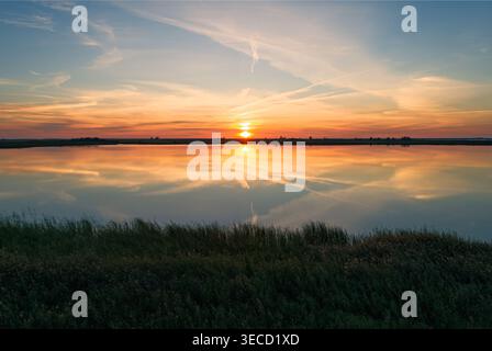 Die Sonne untergeht über dem wunderschönen See und strahlt ein warmes Leuchten über Wasser und Himmel aus Stockfoto