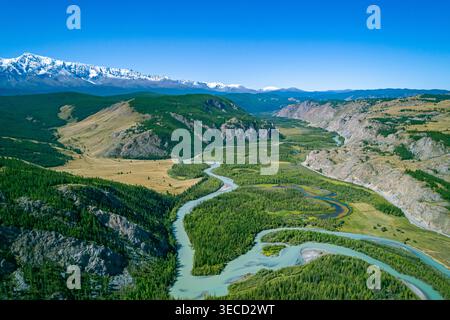 Aus der Vogelperspektive fängt die weite Landschaft des Altai mit einem mäandernden Fluss, üppigen Wäldern und weit entfernten schneebedeckten Bergen an einem klaren Tag ein Stockfoto