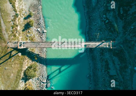 Altai Berglandschaft mit einer robusten Hängebrücke, die sich an einem klaren, sonnigen Tag über einen lebhaften türkisfarbenen Fluss erstreckt Stockfoto
