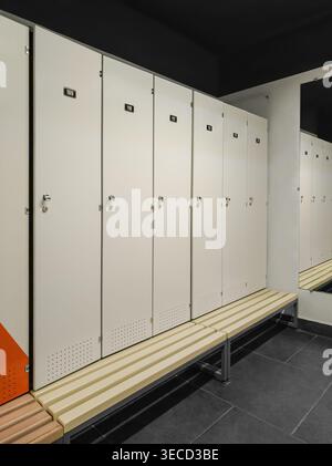 Reihen Sie weiße Schließfächer im Fitnessstudio, im Schwimmbad oder im Umkleideraum der Produktionsanlage. Raum, Umkleideraum für Arbeiter mit individuellen Metallschränken, Bänken Stockfoto