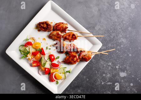 Köstliche gegrillte Fleischspieße mit Sommersalat aus Kirschtomaten, Gurken und roten Zwiebeln. Blick von oben mit Kopierraum. Stockfoto