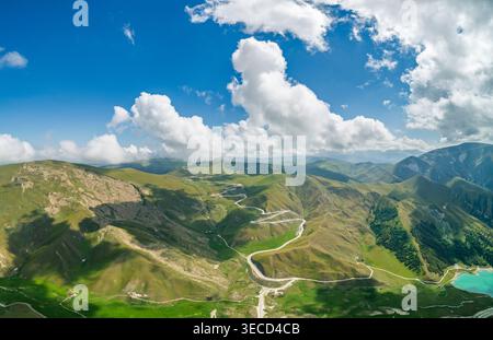 Panoramablick auf die gewundene Bergstraße, die üppige grüne Hänge unter hellem Himmel durchquert Stockfoto
