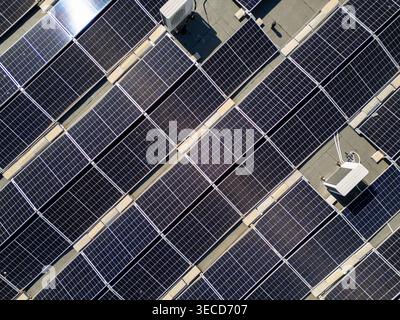 Hochwinklige Drohnenaufnahme einer großen Solarpaneel-Installation auf einem Flachdach. Dolly zoomt vorwärts und zeigt saubere Infrastruktur für erneuerbare Energien und Stockfoto